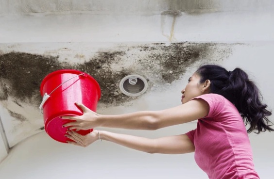 Vrouw vangt lekkend plafond op met emmer